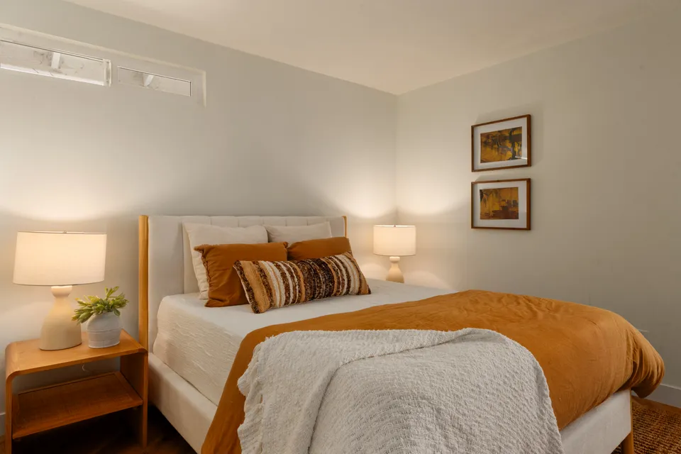 Bedroom with rust orange bedding, wood nightstands and framed prints, Oceanside home