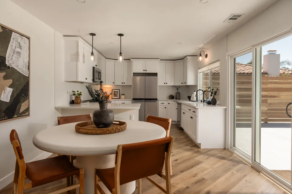 Round dining table with leather chairs beside a white kitchen, Oceanside home