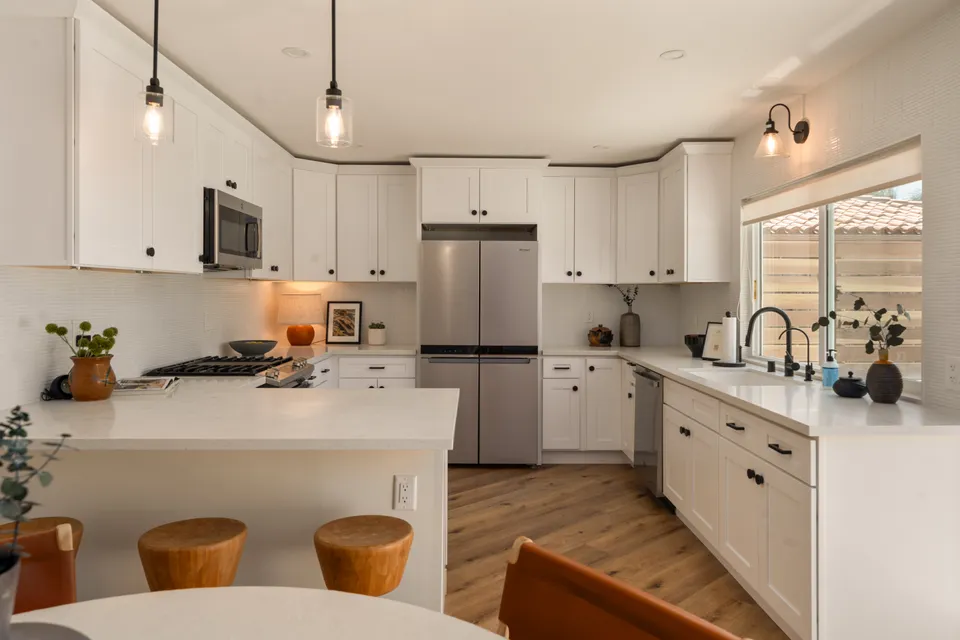 White kitchen with a long counter, pendant lights and wood stools, Oceanside home