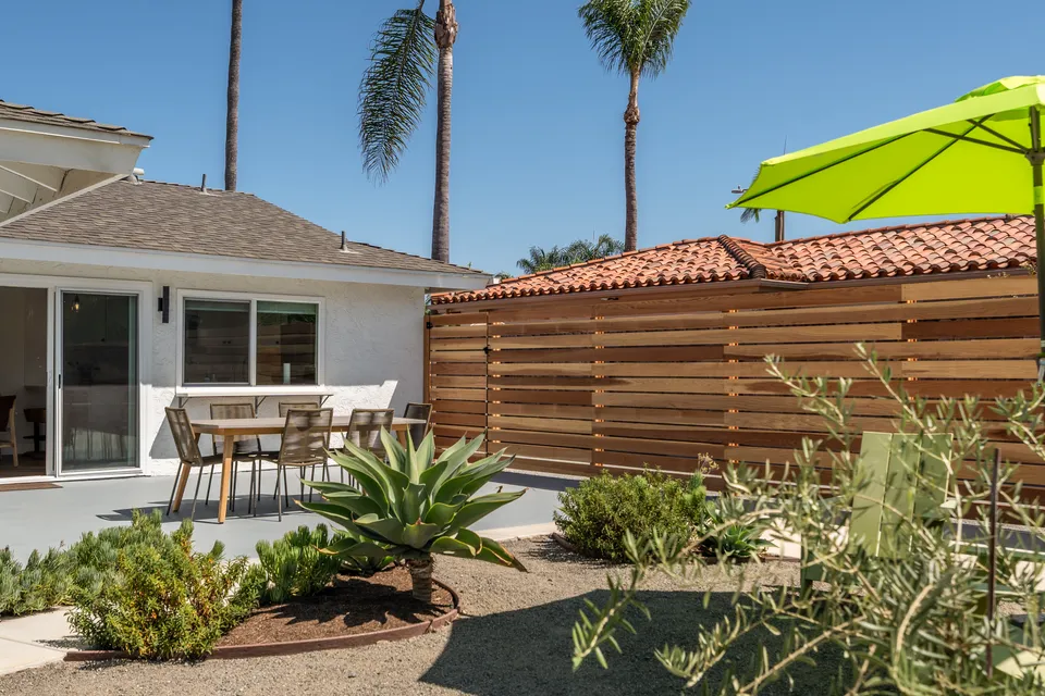 Backyard patio with a dining table, a green umbrella, palms and a wood fence, Oceanside home