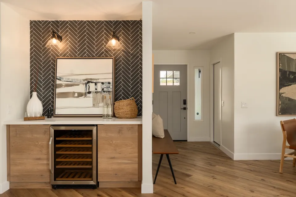 Wet bar with a wine fridge, a black herringbone tile wall and brass sconces, Oceanside home