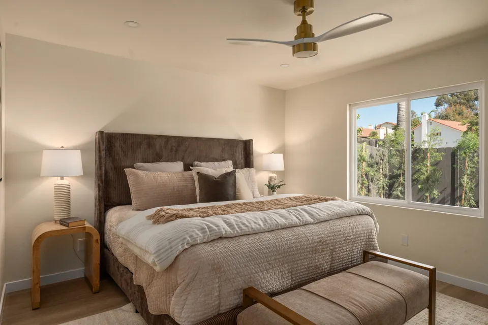 Bedroom with an upholstered headboard, a bench at the foot of the bed and a ceiling fan, renovated San Diego home
