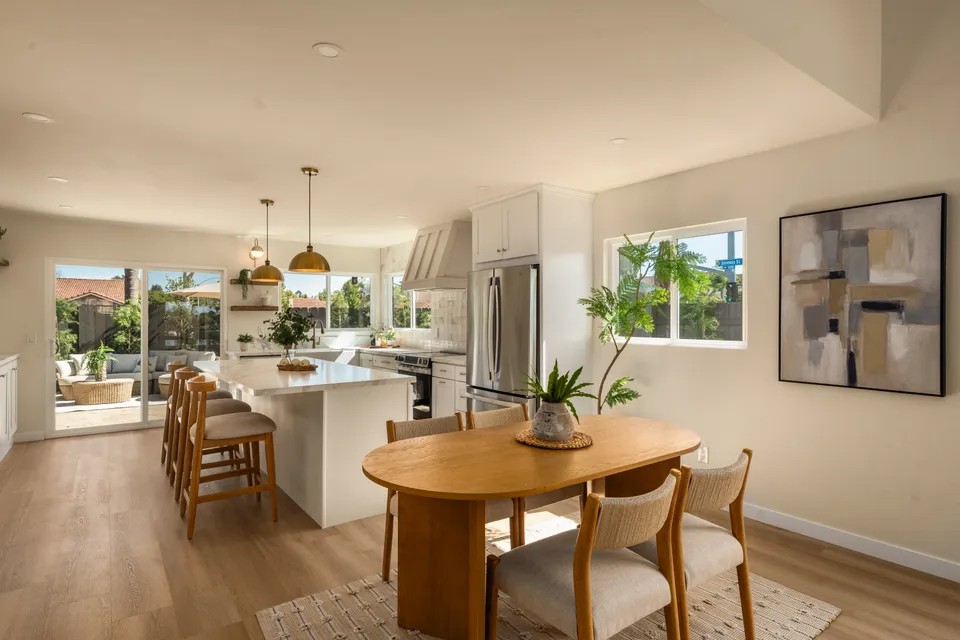 Oval dining table beside a kitchen island with brass pendant lights, renovated San Diego home