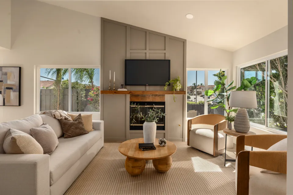 Living room with a paneled fireplace wall, a wood mantel and armchairs by the windows, renovated San Diego home
