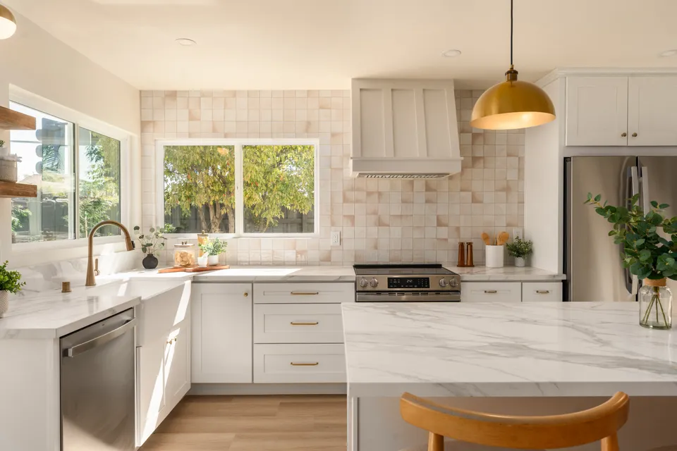 Kitchen with a pale tile backsplash, a white range hood and a brass pendant light, renovated San Diego home