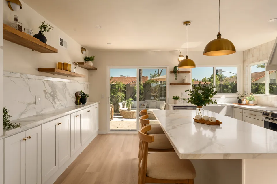 Kitchen with open wood shelves, a white stone backsplash and an island under brass pendants, renovated San Diego home