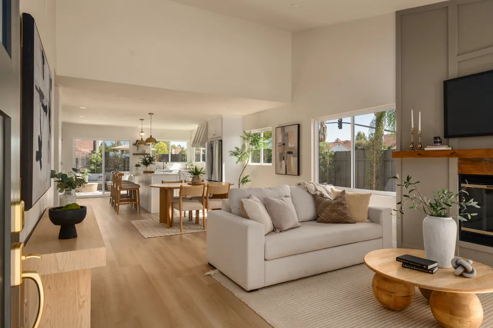 Living room with a fireplace and a round wood coffee table, open to the dining room and kitchen, renovated San Diego home
